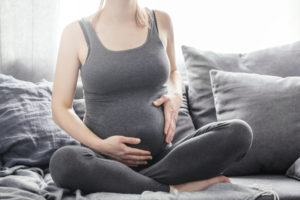 Pregnant woman sitting on couch, relaxing and touching her belly. Enjoying pregnancy. Family baby concept.