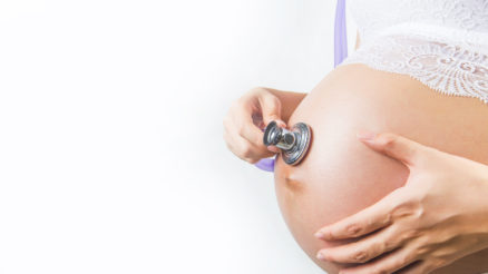 Pregnant woman using stethoscope to check the baby in her belly